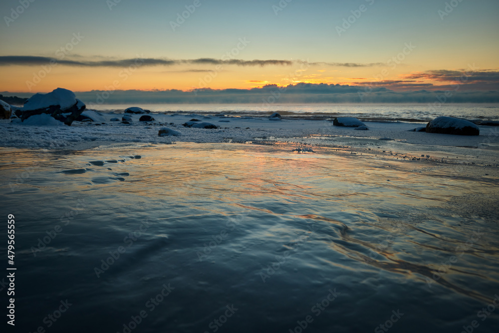 deep snow over rocks at the beach in cold winter sunset by the sea
