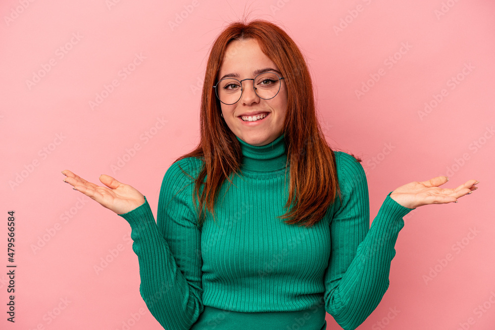 Young caucasian woman isolated on pink background makes scale with arms, feels happy and confident. Young caucasian woman isolated on pink background makes scale with arms, feels happy and confident.