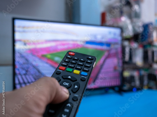 Close up of hand holding a remote control to LCD TV at home.