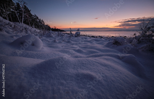 deep snow over rocks at the beach in cold winter sunset by the sea with pine trees and spruce