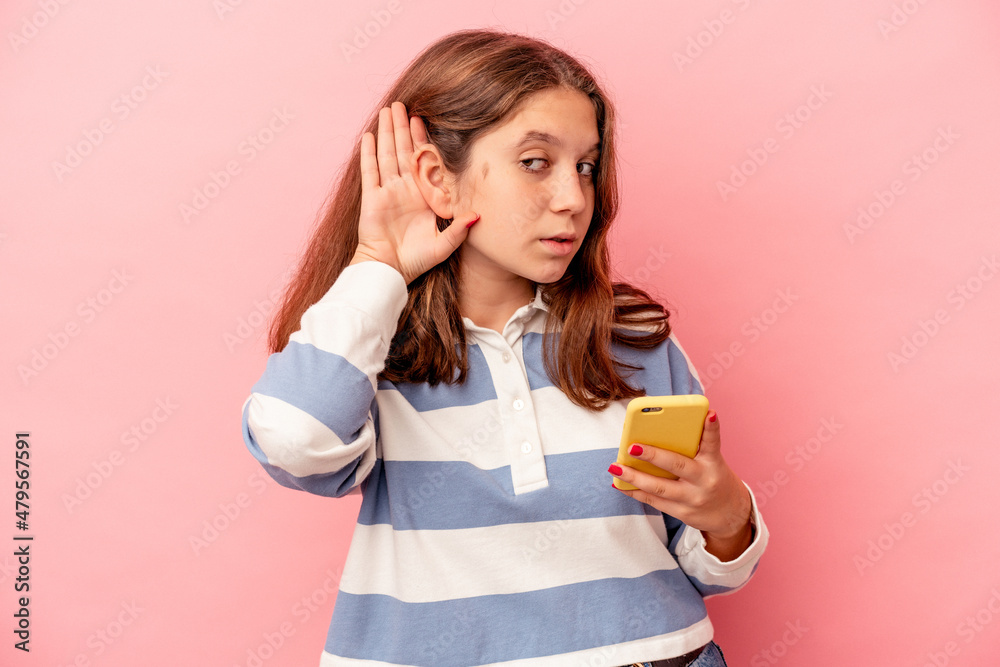 Little caucasian girl holding mobile phone isolated on pink background trying to listening a gossip. Little caucasian girl holding mobile phone isolated on pink background trying to listening a gossip.