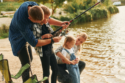 Learning to fishing. Father and mother with son and daughter together outdoors at summertime