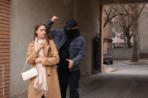 Criminal attacking young woman in alley, space for text. Self defense concept photo