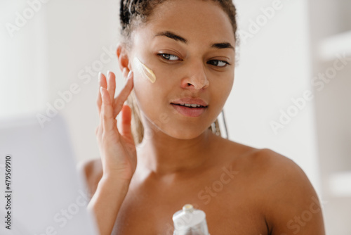 Young black woman applying face cream looking in mirror photo