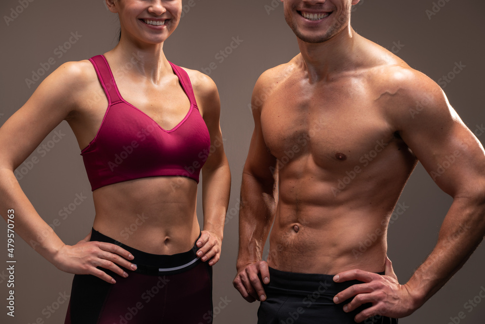 Fototapeta premium Cropped view of the athletic man and woman posing to the camera before fitness exercise at the studio with brown wall