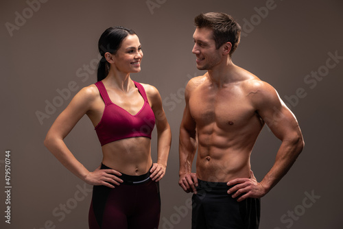 Bodybuilding. Strong man and woman with well shaped bodies looking at each other while posing isolated on brown background