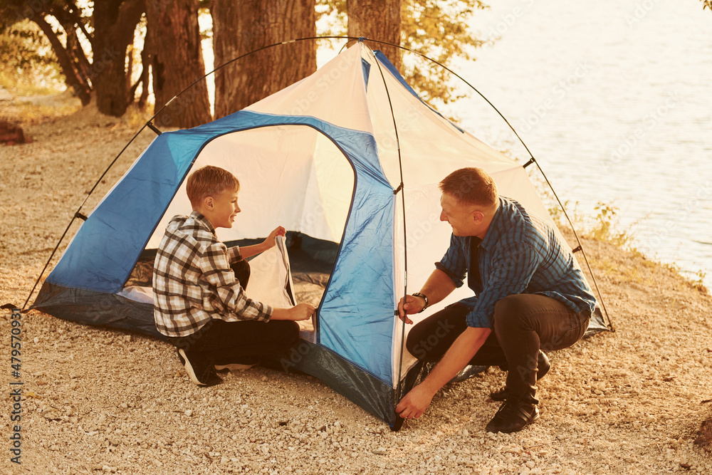 Father and son installing tent outdoors near the lake
