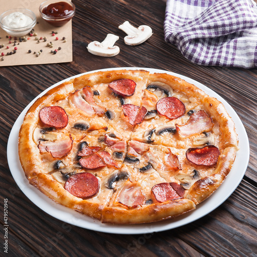 Meat pizza with sausages and cheese lies on a white plate on a wooden table