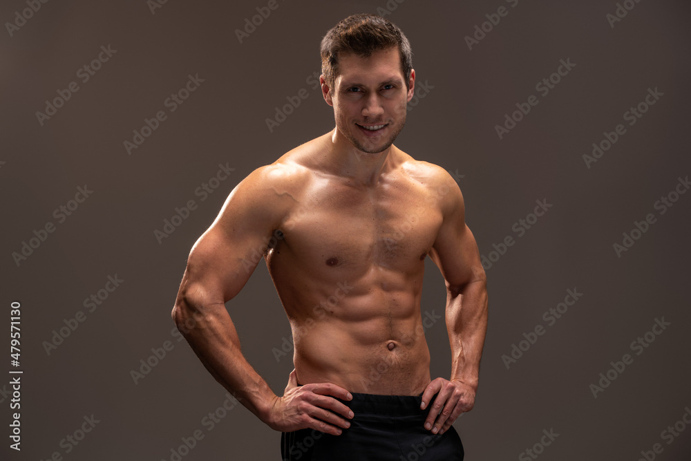 Horizontal view of the handsome muscular guy posing isolated on brown background, while showing his strong body and muscles