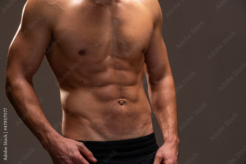 Close up view of the young handsome male athlete showing muscles isolated on a dark background. Sport and bodybuilding concept