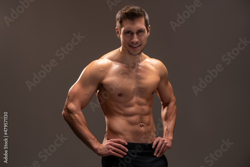 Horizontal view of the handsome muscular guy posing isolated on brown background, while showing his strong body and muscles