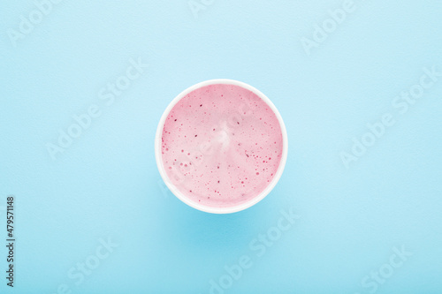 White paper cup of berry ice cream on light blue table background. Pastel color. Closeup. Cold sweet snack in summer. Top down view.