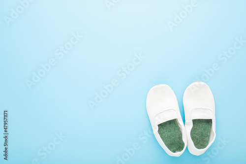 White new leather gymnastic slippers on light blue table background. Pastel color. Closeup. Child shoes for sport lesson in kindergarten. Empty place for text. Top down view.