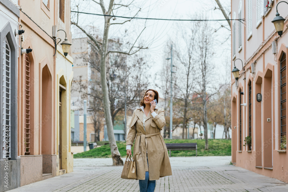 Fototapeta premium Woman talking on the phone while walking down the street.