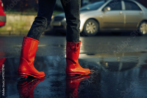 Woman with red rubber boots walking in puddle, closeup. Rainy weather