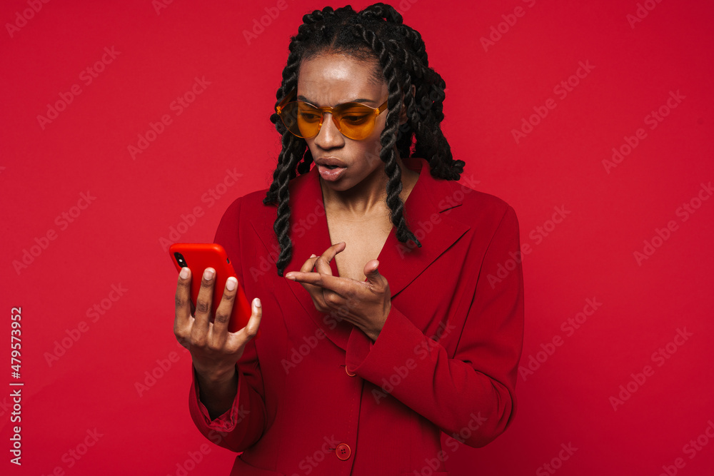 Black young woman frowning while pointing finger at her cellphone Black young woman frowning while pointing finger at her cellphone