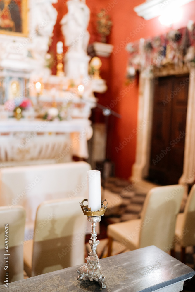 Candle in a silver candlestick stands on the table near the altar in the church