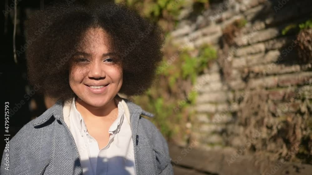 Close up Fashion street style portrait of attractive young natural beauty African American woman with afro hair in blue coat posing walking outdoors in sunny day. Happy lady with perfect teeth smile Close up Fashion street style portrait of attractive young natural beauty African American woman with afro hair in blue coat posing walking outdoors in sunny day. Happy lady with perfect teeth smile
