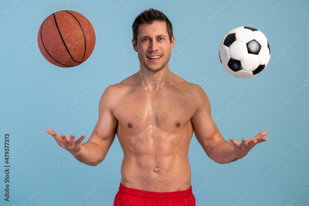 Young sports man posing with balls of basketball and football over isolated blue wall with excited expression. Stock photo