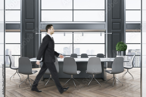 Businessman walking in modern wooden and concrete meeting room interior with panoramic city view, furniture and daylight. Success and workplace concept.