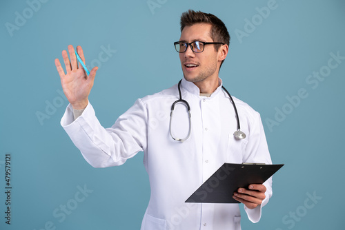 Medical care and prescription concept. Male medicine doctor holding open clipboard and waving with hand to somebody in front of the camera