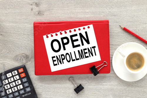 Open Enrollment. wood office desk with notepad, red diary, stationery, coffee cup.