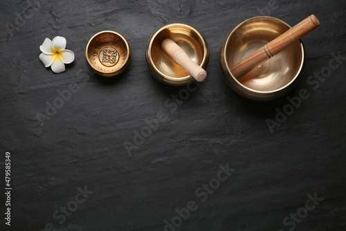 Golden singing bowls, mallets and flower on black table, flat lay. Space for text