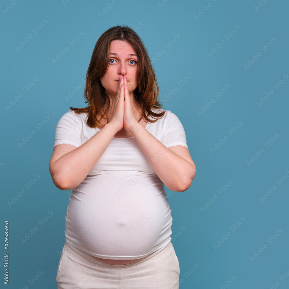 Prayer gesture with hands of pregnant woman, studio shot on blue background Prayer gesture with hands of pregnant woman, studio shot on blue background