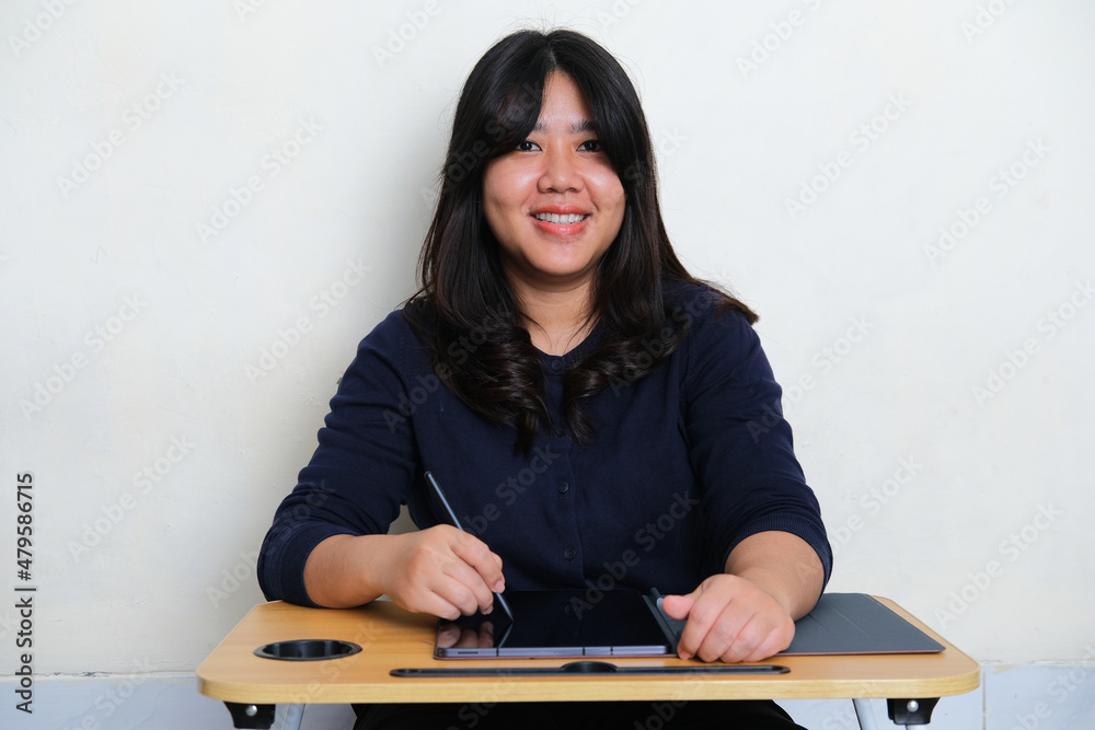 Young Asian woman smiling to the camera when working using mobile tablet