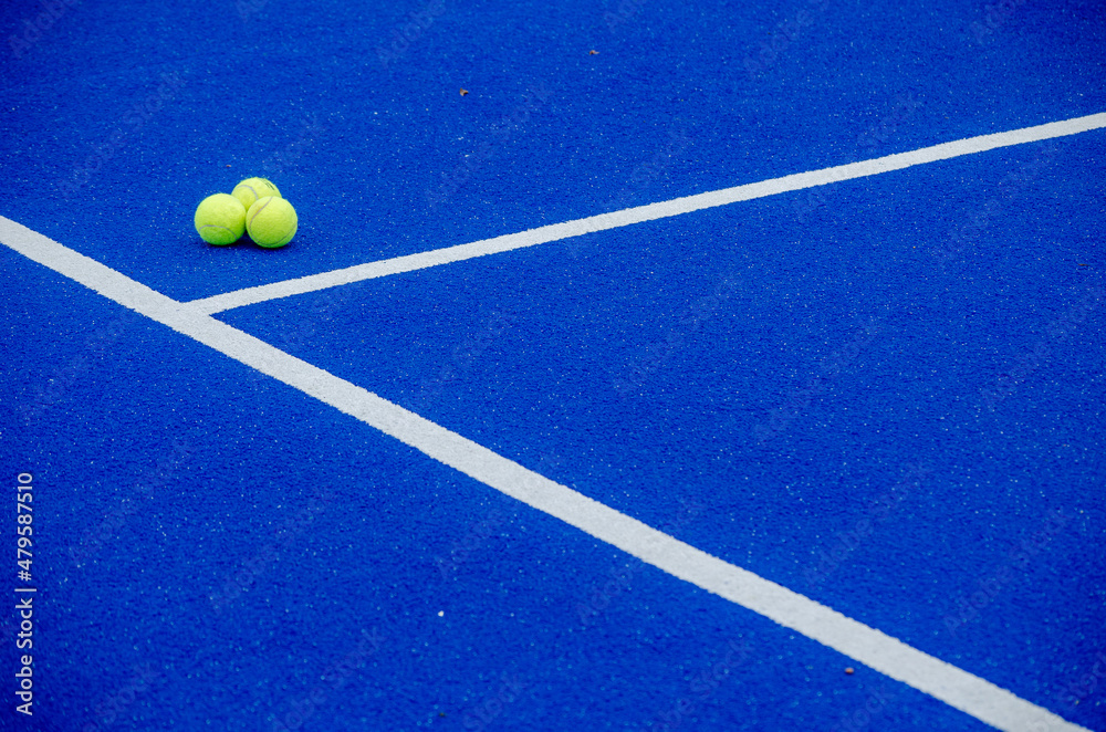Three paddle tennis balls on a blue synthetic grass paddle tennis court surface