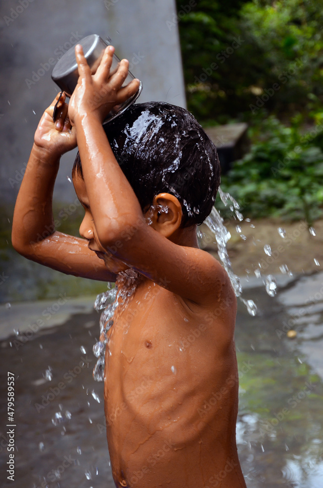 Fototapeta premium Closeup of a child taking bath with a mug. A kid pouring water with a jug and splashing water over head.