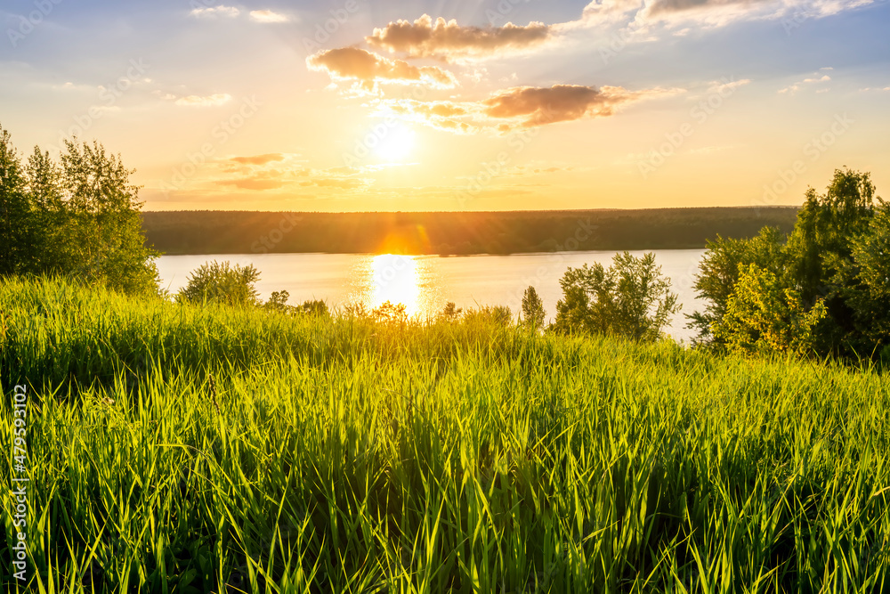 scenic view at nice landscape on a beautiful lake and colorful sunset with reflection on water with green gras on foreground and glow on a background, spring season landscape