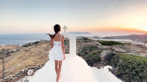 young girl woman in a white dress walking romantic resort walks through a traditional typical Greek church sunset, by famous landmark destination Cyclades Island, Greece