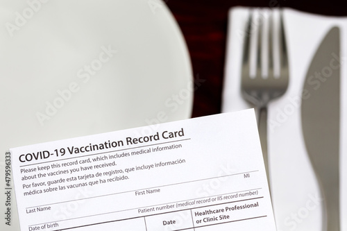 Covid-19 vaccination card and restaurant table. Indoor vaccine mandate, entertainment restrictions and vaccination requirement concept.