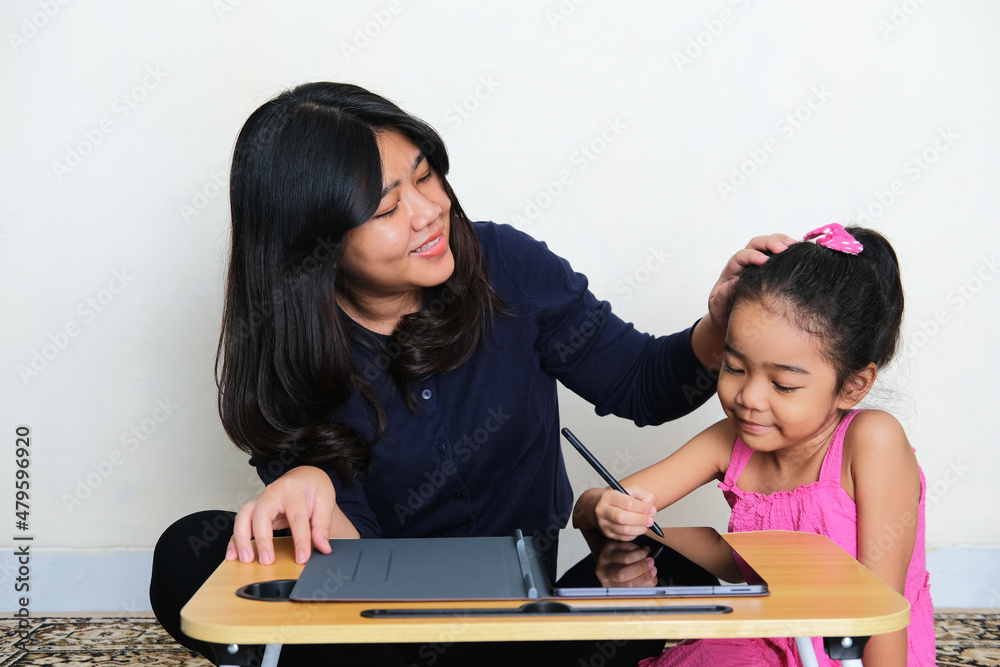 A mother smiling happy when accompany her daughter during study using mobile tablet gadget A mother smiling happy when accompany her daughter during study using mobile tablet gadget