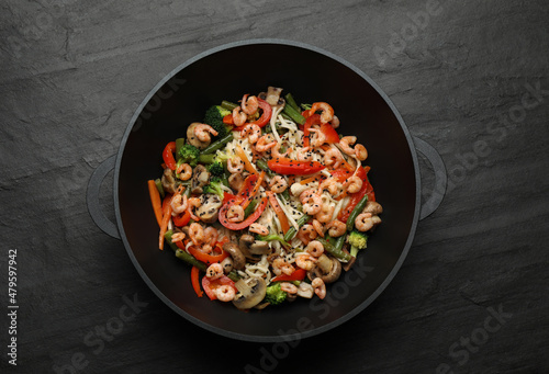Stir fried noodles with mushrooms, shrimps and vegetables in wok on black table, top view