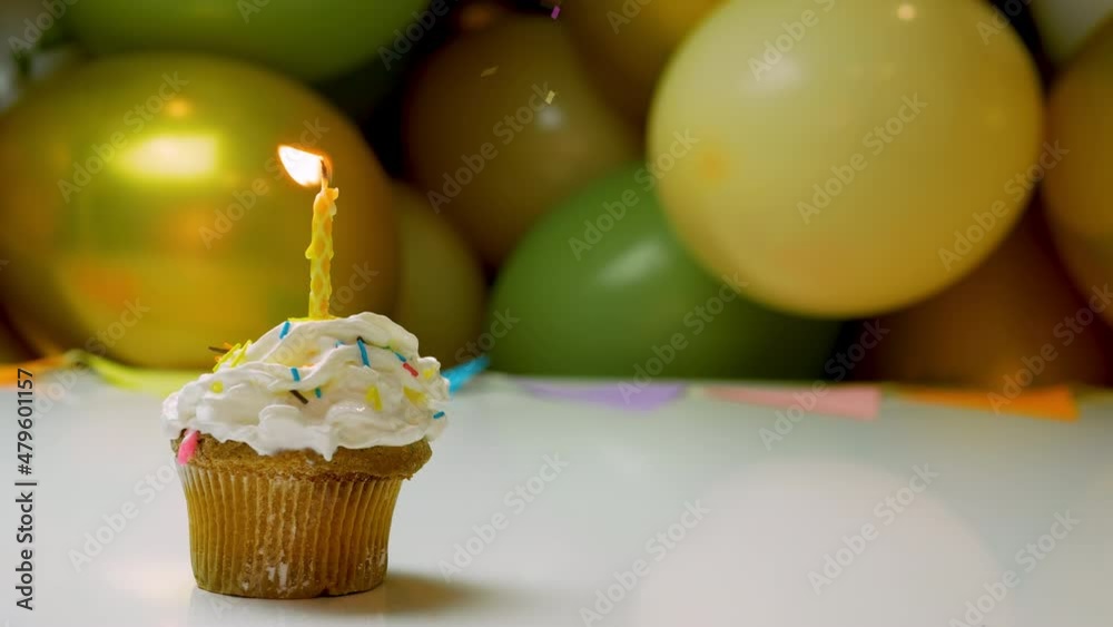 Festive birthday background, cream cupcake with burning candle and balloons in the background. Birthday video background for any age copy space.