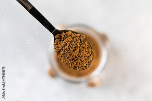 A small spoon with instant coffee granules over a glass jar of coffee.