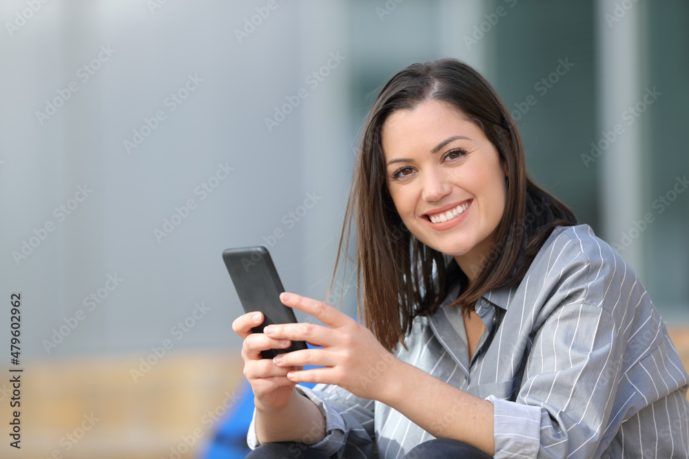 Happy student holding phone looks at you Happy student holding phone looks at you