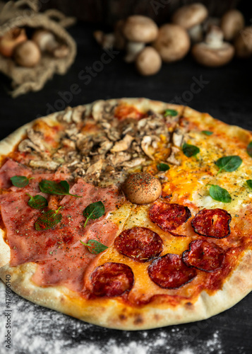 Italian Pizza Four Seasons (Pizza Quattro Stagioni) with different ingredients on the wooden table in the kitchen
