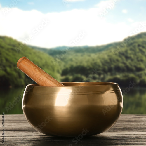 Golden singing bowl and mallet on wooden table against mountain landscape