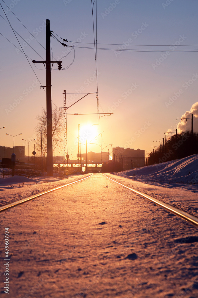 Beautiful snow-covered railway in the rays of the setting sun. The rails are heavily covered in snow.