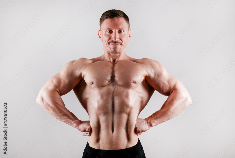 Professional bodybuilder posing over isolated white background. Front Lat Spread pose. Studio shot of a fitness trainer flexing the muscles. Close up, copy space.