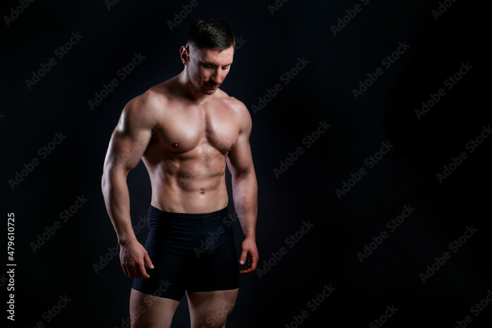 Professional bodybuilder posing over isolated black background. Studio shot of a fitness trainer flexing the muscles. Close up, copy space.