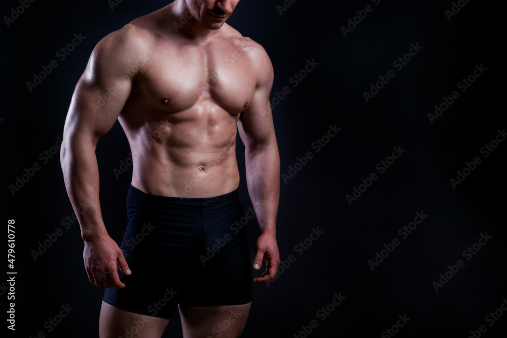 Professional bodybuilder posing over isolated black background. Studio shot of a fitness trainer flexing the muscles. Close up, copy space.