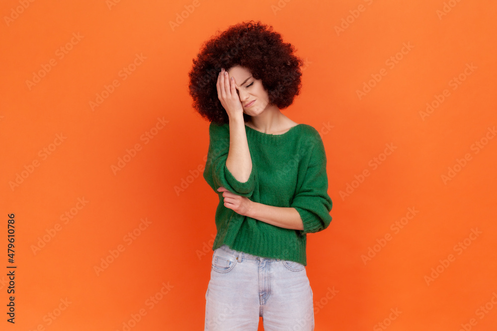 Sad woman with Afro hairstyle wearing green sweater making facepalm gesture keeping hand on head, blaming herself for bad memory, unforgivable mistake. Indoor studio shot isolated on orange background Sad woman with Afro hairstyle wearing green sweater making facepalm gesture keeping hand on head, blaming herself for bad memory, unforgivable mistake. Indoor studio shot isolated on orange background