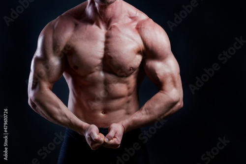 Professional bodybuilder posing over isolated black background. Studio shot of a fitness trainer flexing the muscles in an aggressive pose. Close up, copy space.