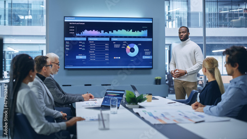 Office Conference Room Meeting Presentation: Black Businessman Talks, Uses TV Screen to Show Company Growth with Big Data Analysis, Graphs, Charts, Infographics. e-Commerce e-Business.