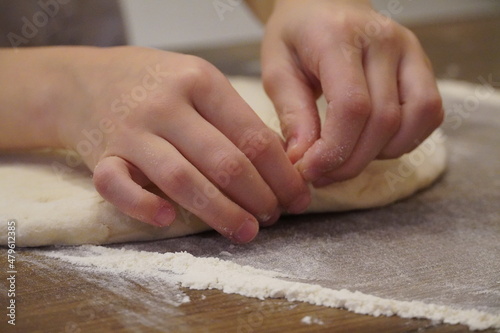 Young hands pinch and crumple the dough on a brown wooden table sprinkled with flour.