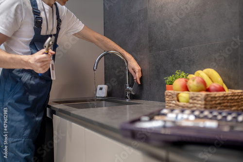 Fototapeta Naklejka Na Ścianę i Meble -  Plumber hand opening water tap in kitchen